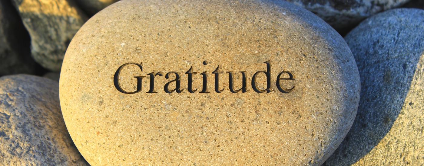 A pebble on a beach inscribed with the word gratitude.